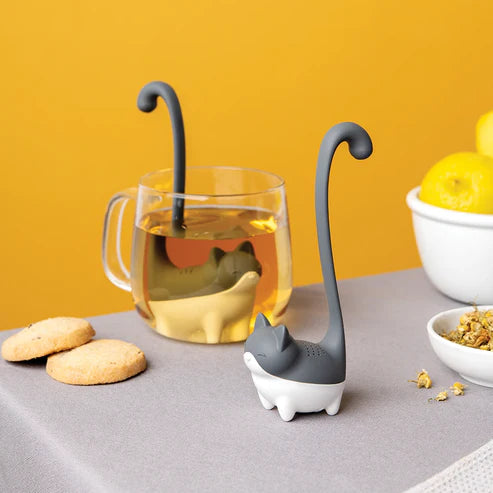 Cat-shaped tea infuser with a glass of tea and cookies on a yellow background