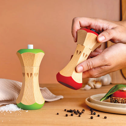 Wooden salt and pepper shakers with a hand holding one, on a wooden surface.