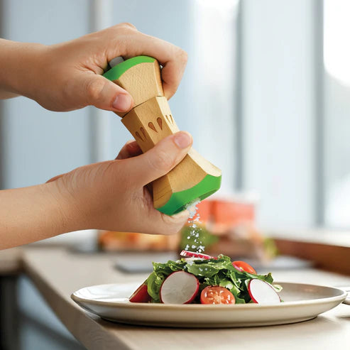 Person seasoning a salad with a wooden salt grinder shaped like a radish.